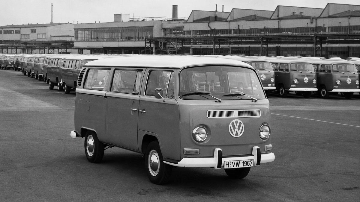 Black and white image of a 1967 VW T2 parked in a factory car park with rows of other Volkswagen campers waiting to be shipped.