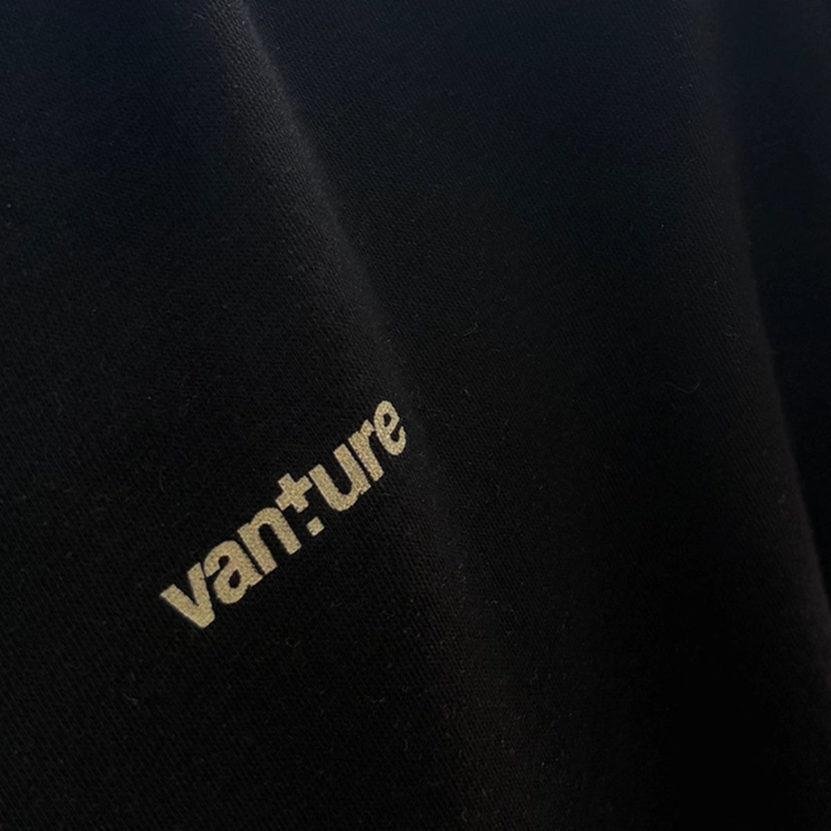 Close-up of black Vanture Beginning Hoodie fabric showing the Vanture chest print