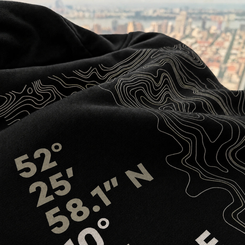 Close-up of the Vanture Beginning Hoodie showing the Wolfsburg coordinates and topographic print