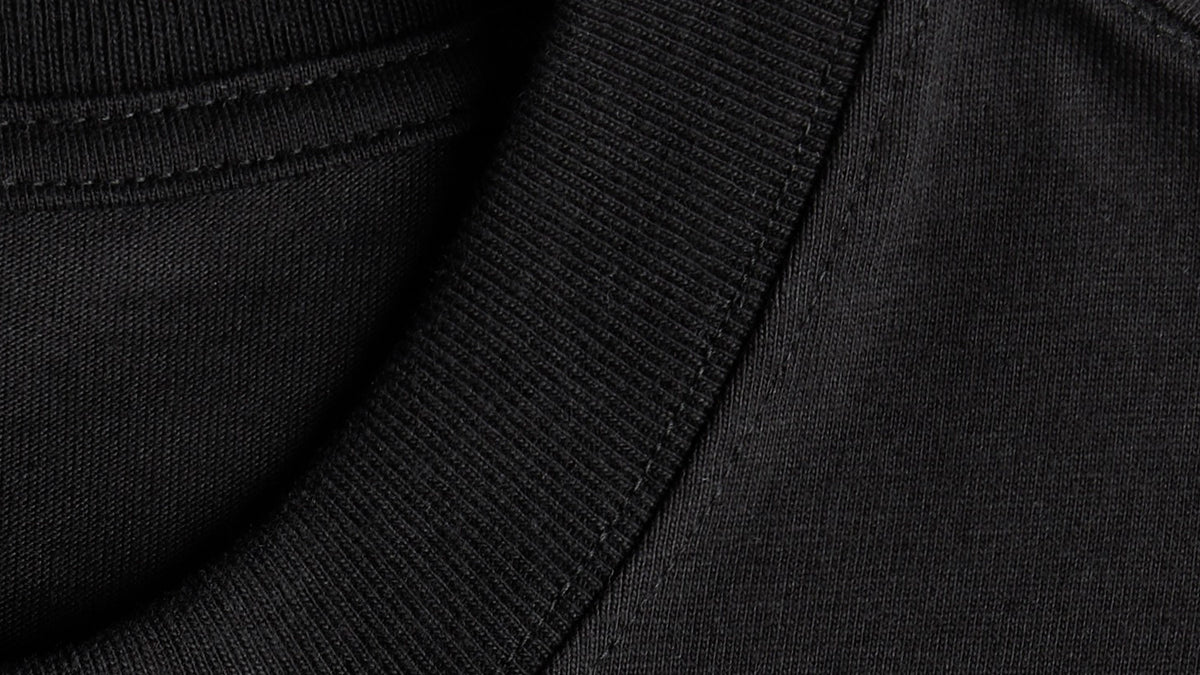 Close-up detail of black heavyweight cotton T-shirt fabric showing the ribbed collar and material texture.