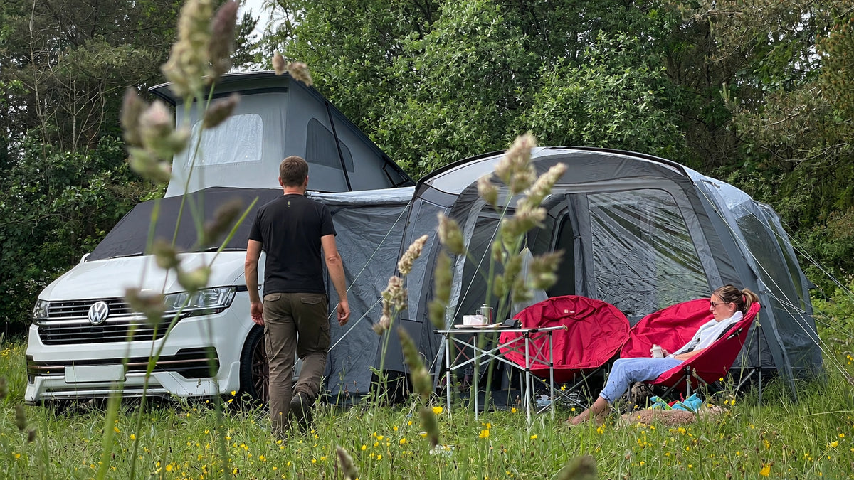 VW campervan with an attached awning at a woodland campsite, with a person relaxing outside.